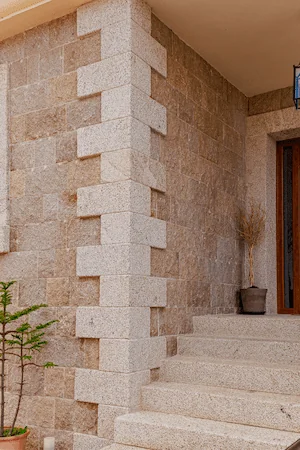 Entrada de vivienda revestida con granito rubio abujardado y acabado rústico.