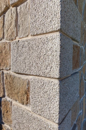 Esquinas de muro en granito rubio con textura abujardada artesanal.