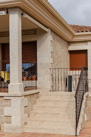 Escalera, columna y zócalo en granito rubio abujardado, combinación armoniosa para exteriores.